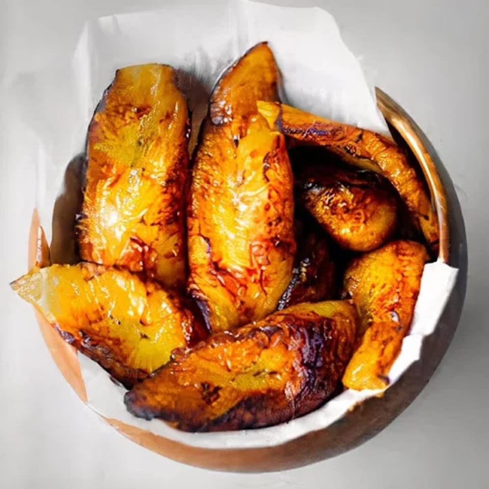 A wooden bowl filled with golden-brown, caramelized Jamaican fried plantains, lined with white parchment paper.