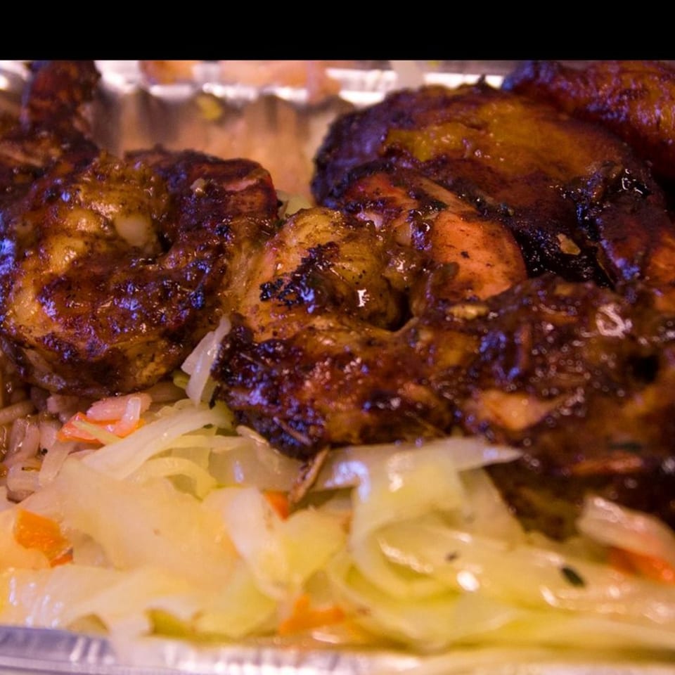 Close-up of Just Jerk's jerk chicken and shrimp with rice and cabbage in a foil container.