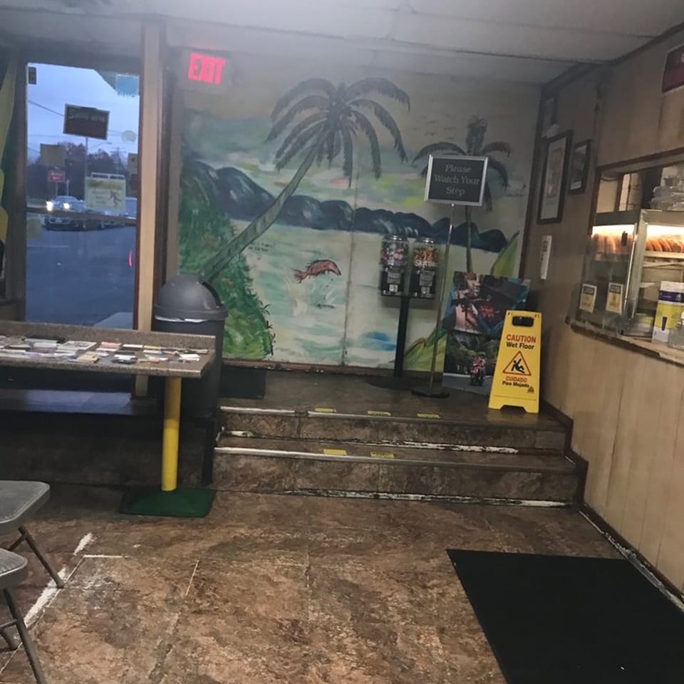 Interior of Just Jerk restaurant with a Jamaican-themed mural, steps, and a counter.