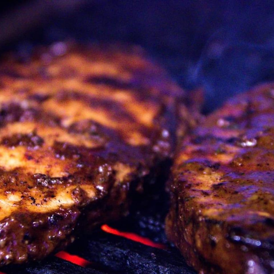Two pieces of Jerk chicken cooking on a grill with glowing red coals.
